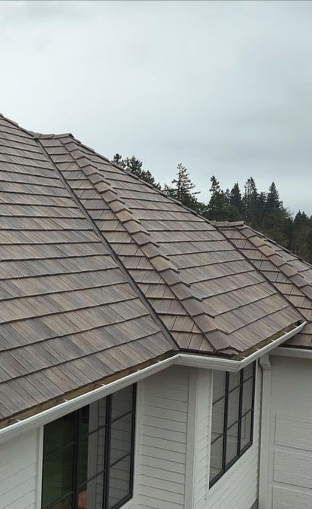 Roof with brown textured shingles on a modern home surrounded by trees.