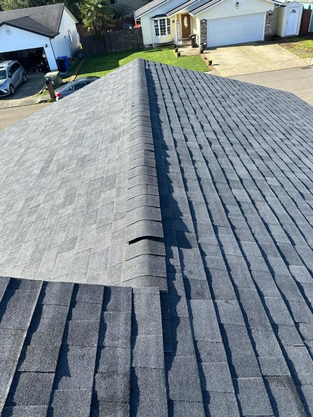 Aerial view of a residential roof showcasing gray asphalt shingles and a clean ridge line.