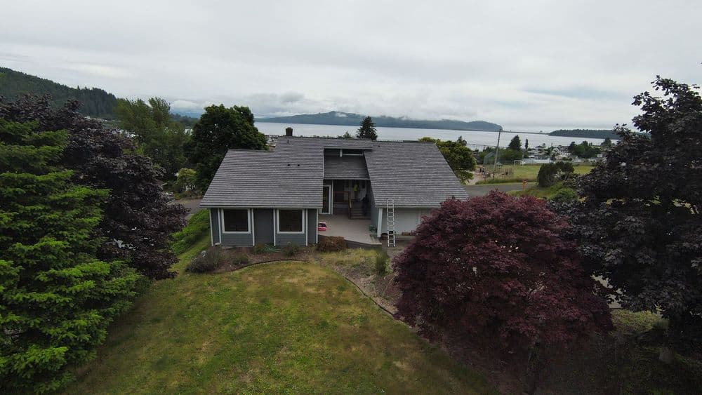 Aerial view of a modern home surrounded by trees, with a lake and mountains in the background.