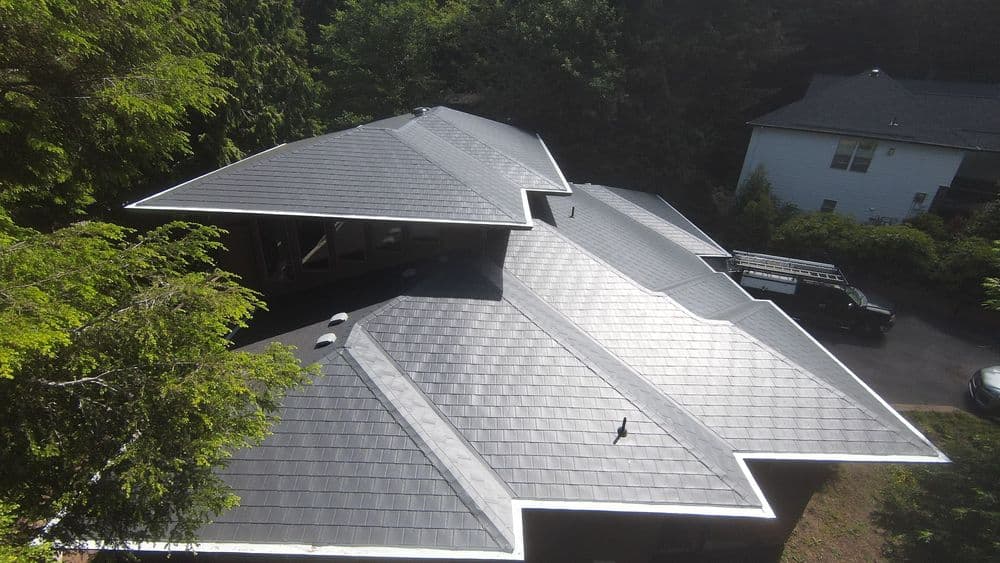 Aerial view of a modern home with a unique multi-slope roof and lush surroundings.