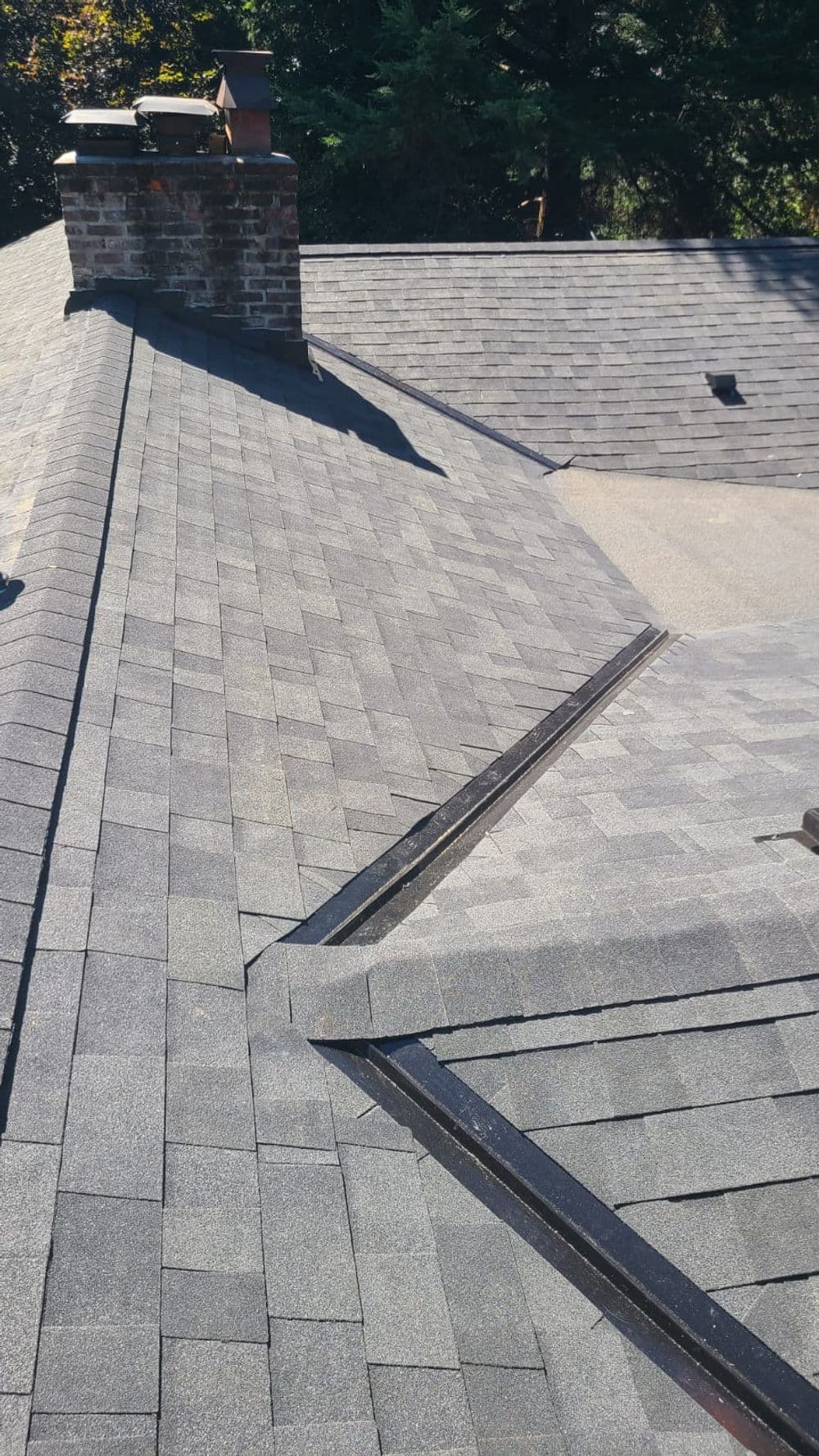 New asphalt shingle roof with a chimney and clean lines under natural sunlight.