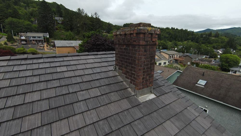 Chimney on a shingled roof with a mountainous backdrop and overcast sky.
