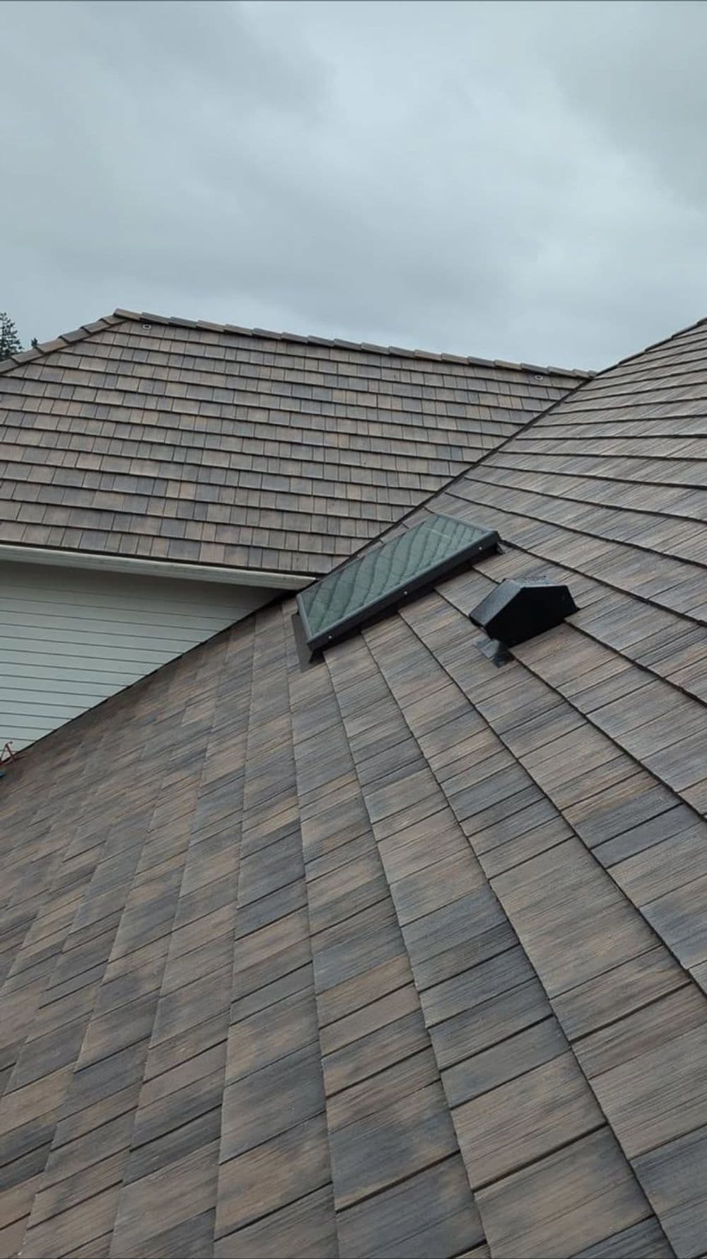 Newly installed shingle roof with a skylight and ventilation system against a cloudy sky.