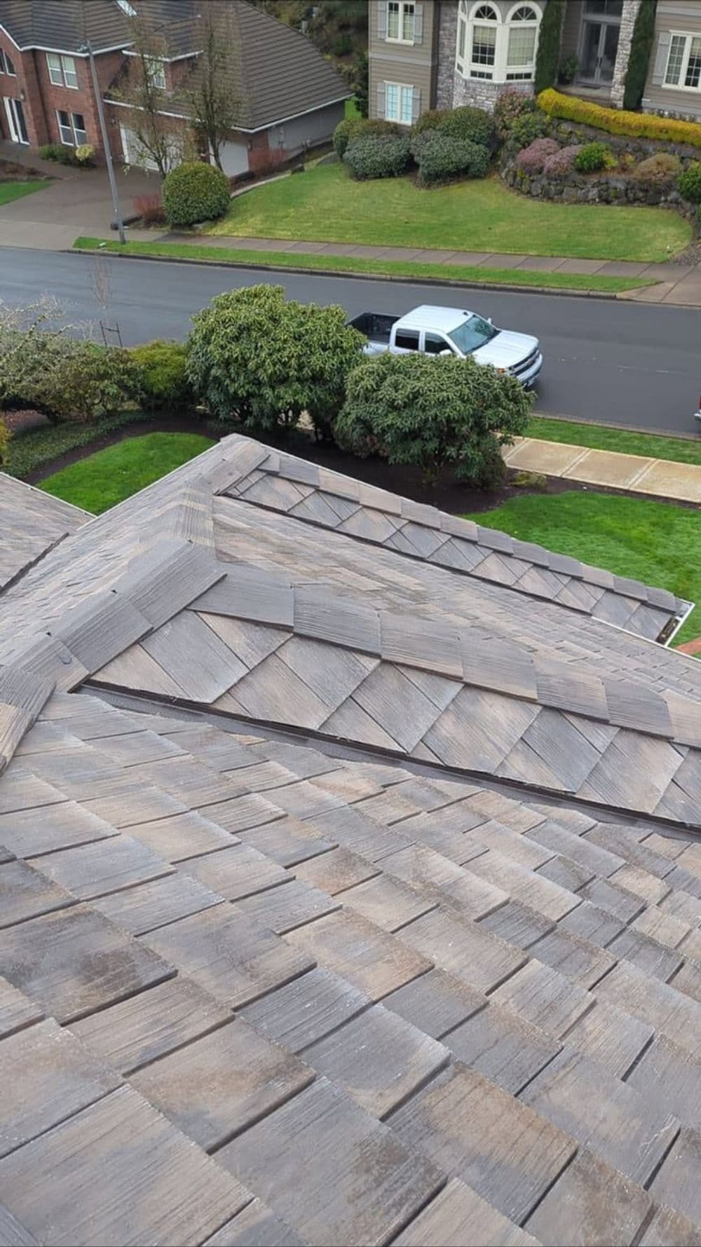 Aerial view of a house roof with wooden shingles and green landscaping.