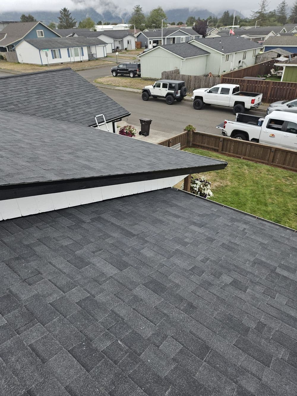 Aerial view of residential roofs with asphalt shingles and nearby parked vehicles.