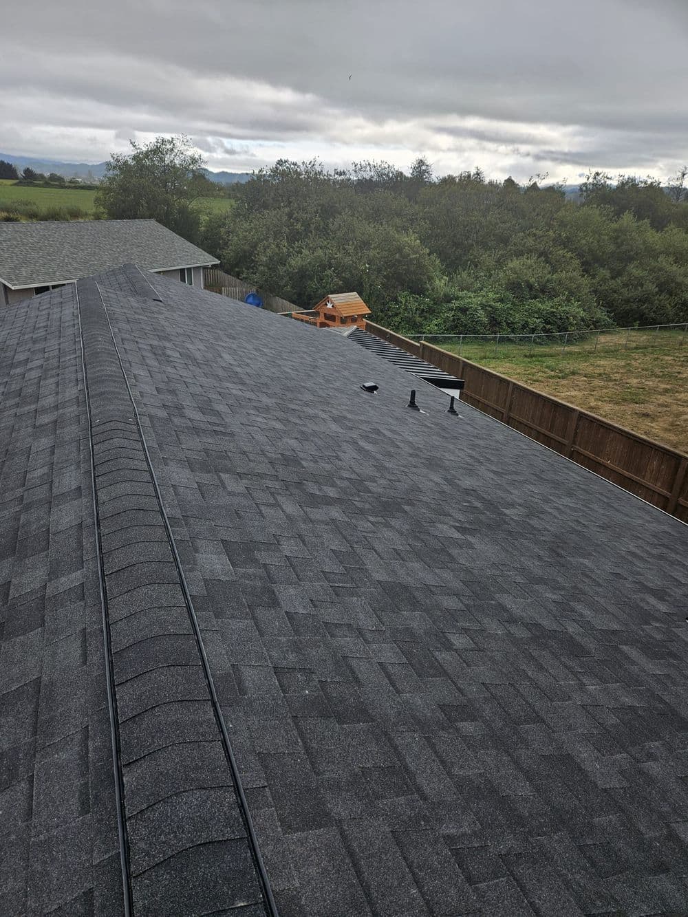 Aerial view of a residential roof with dark shingles and cloudy sky in the background.