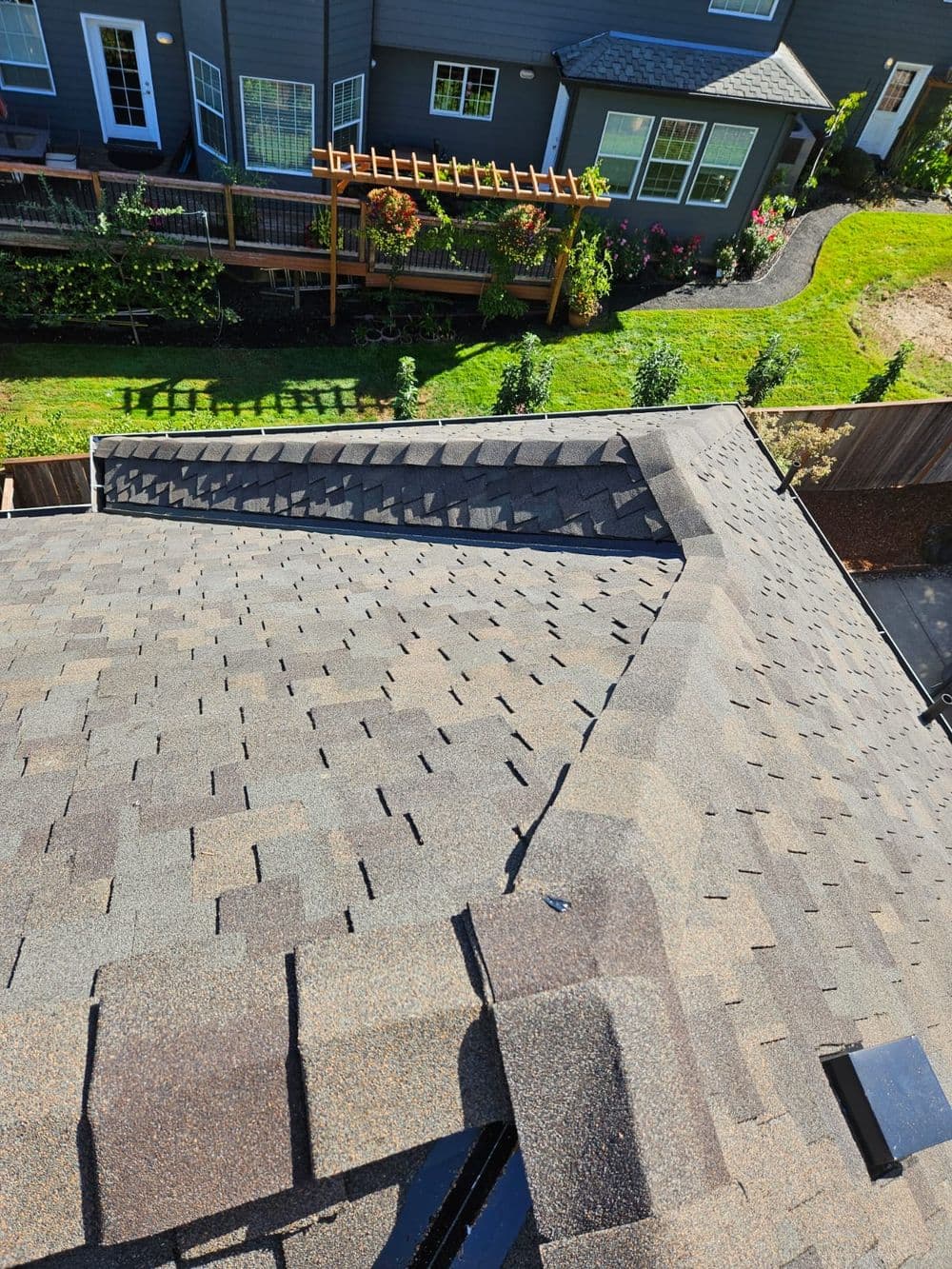 Aerial view of a gray shingle roof with a landscaped yard and house in the background.