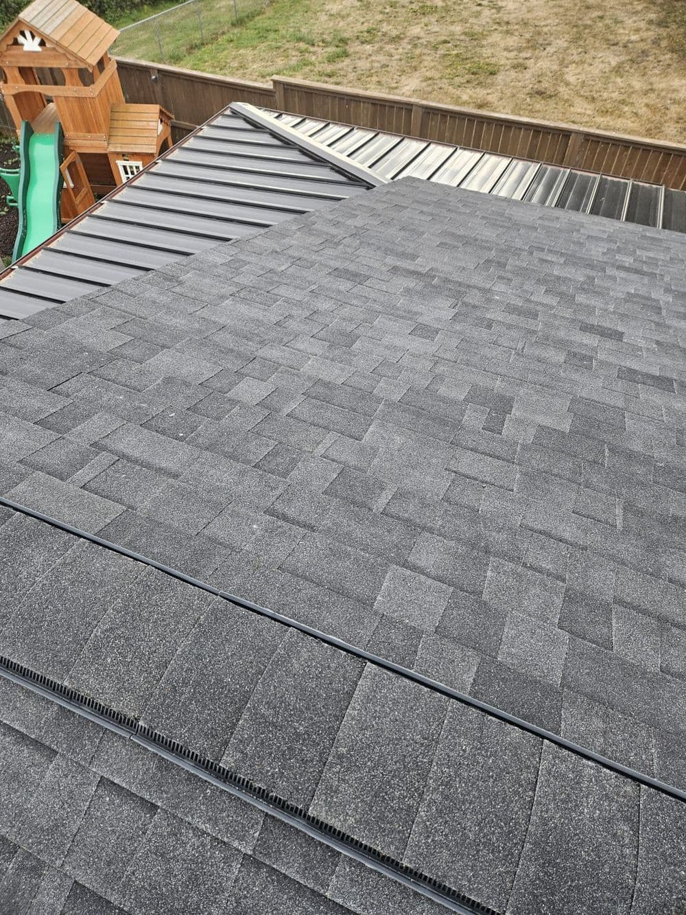 Aerial view of dark shingle and metal roofs on residential buildings in a backyard setting.