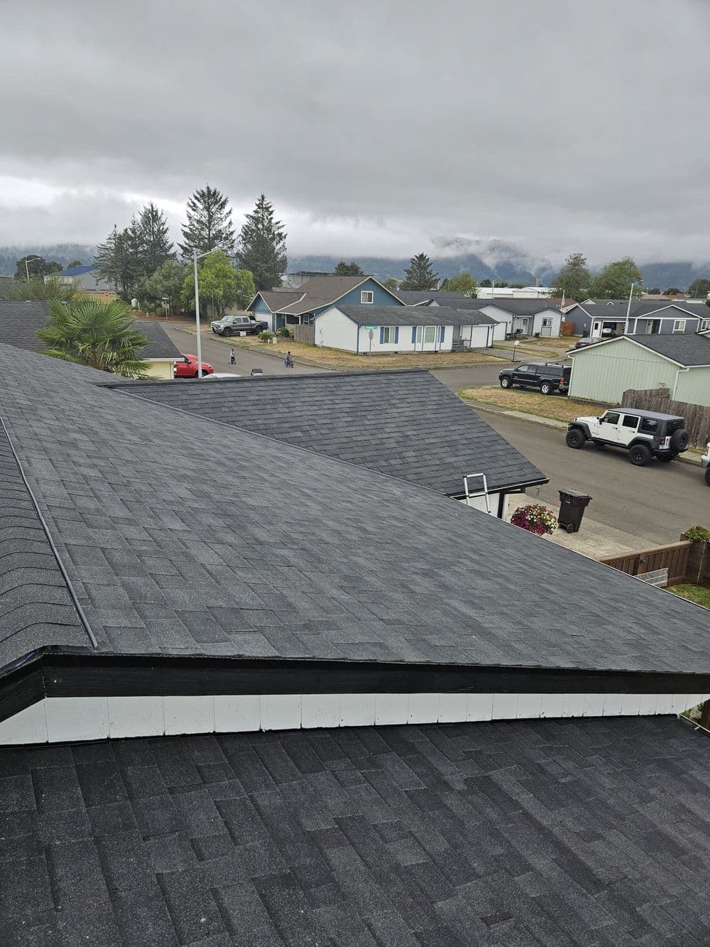 View of asphalt shingle roof over suburban houses under cloudy sky.