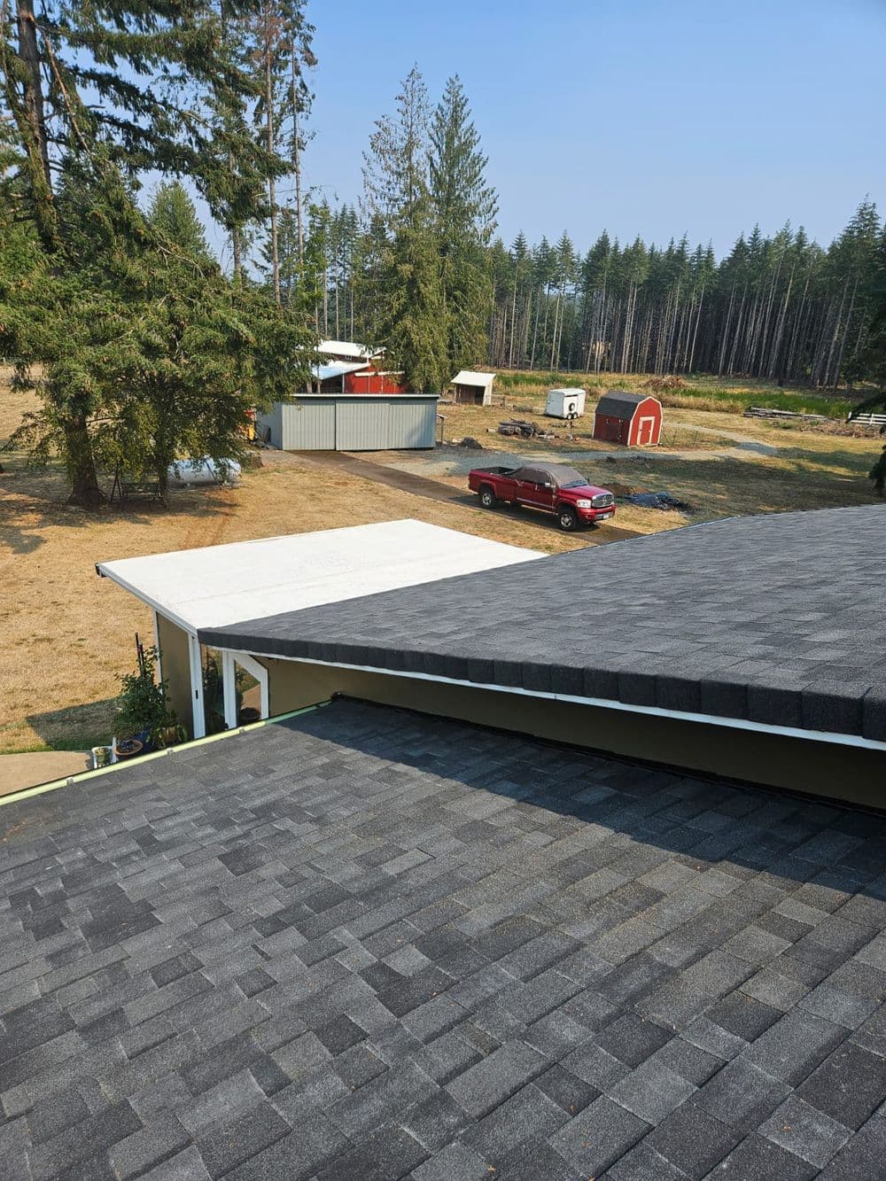 Aerial view of a gray shingle roof with a red truck and farmland in the background.