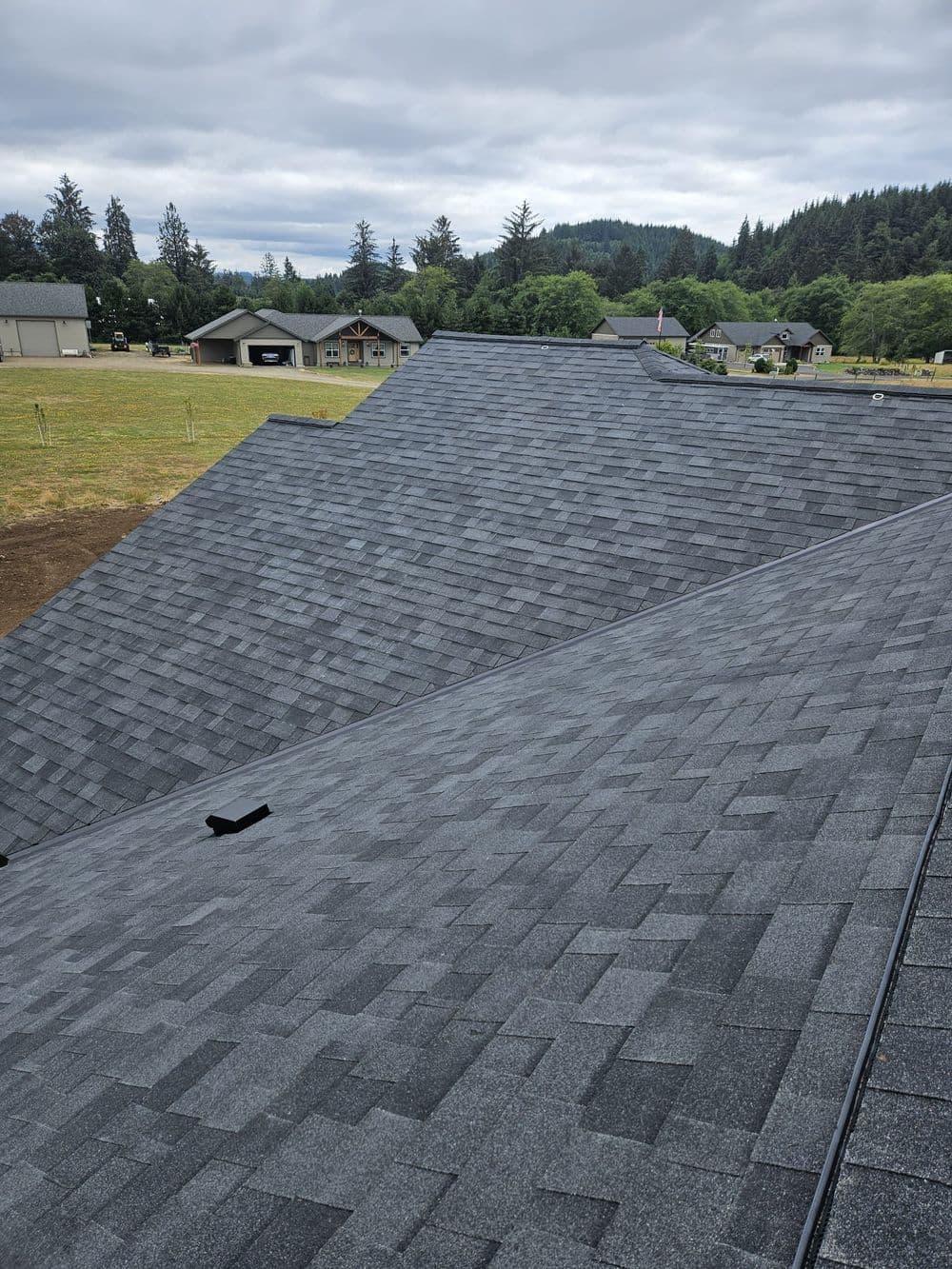 Newly installed gray asphalt shingles on sloped residential roofs with overcast sky backdrop.
