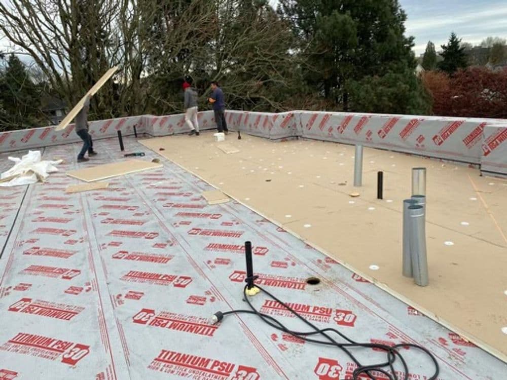 Workers installing roofing materials on a flat roof with a red underlayment.