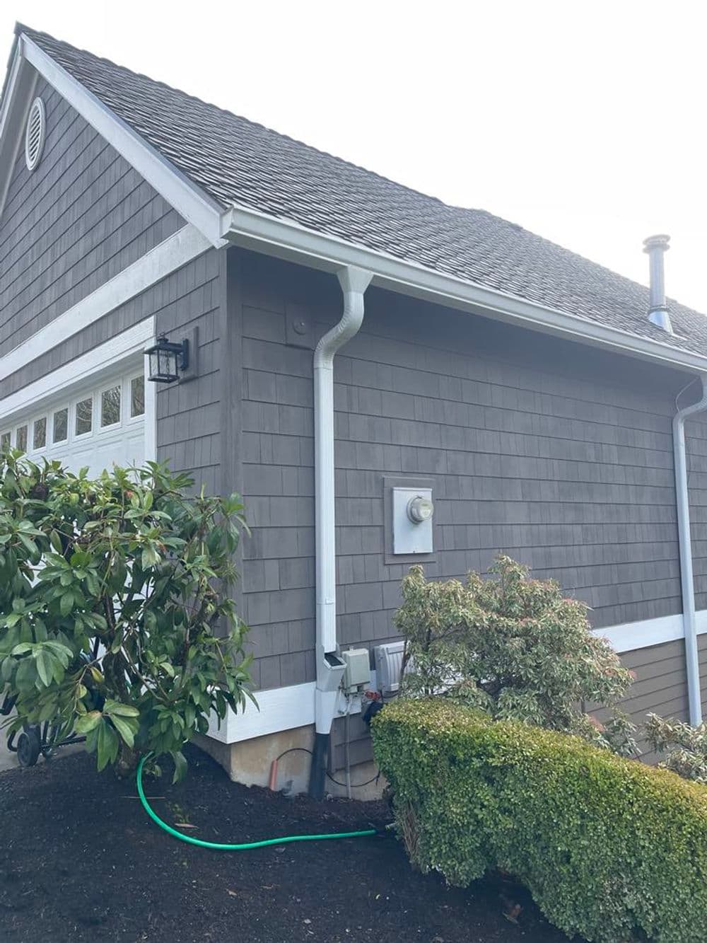 Gray house exterior featuring a side view, landscaping, and utility connections.