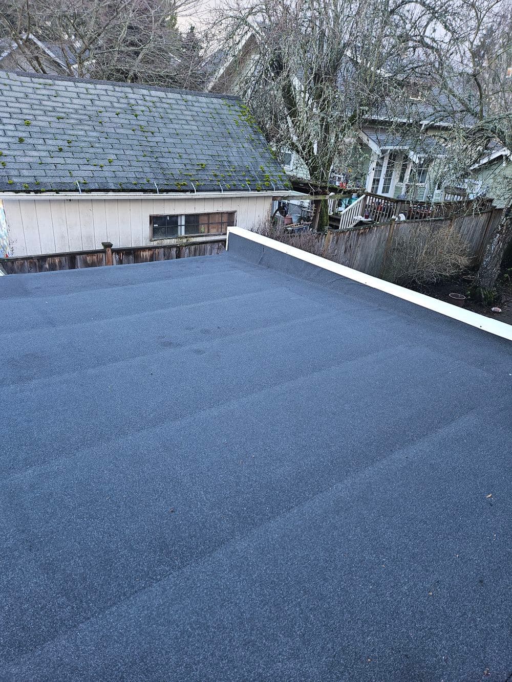 Flat roofing surface on a residential home, showcasing shingles and adjacent buildings.