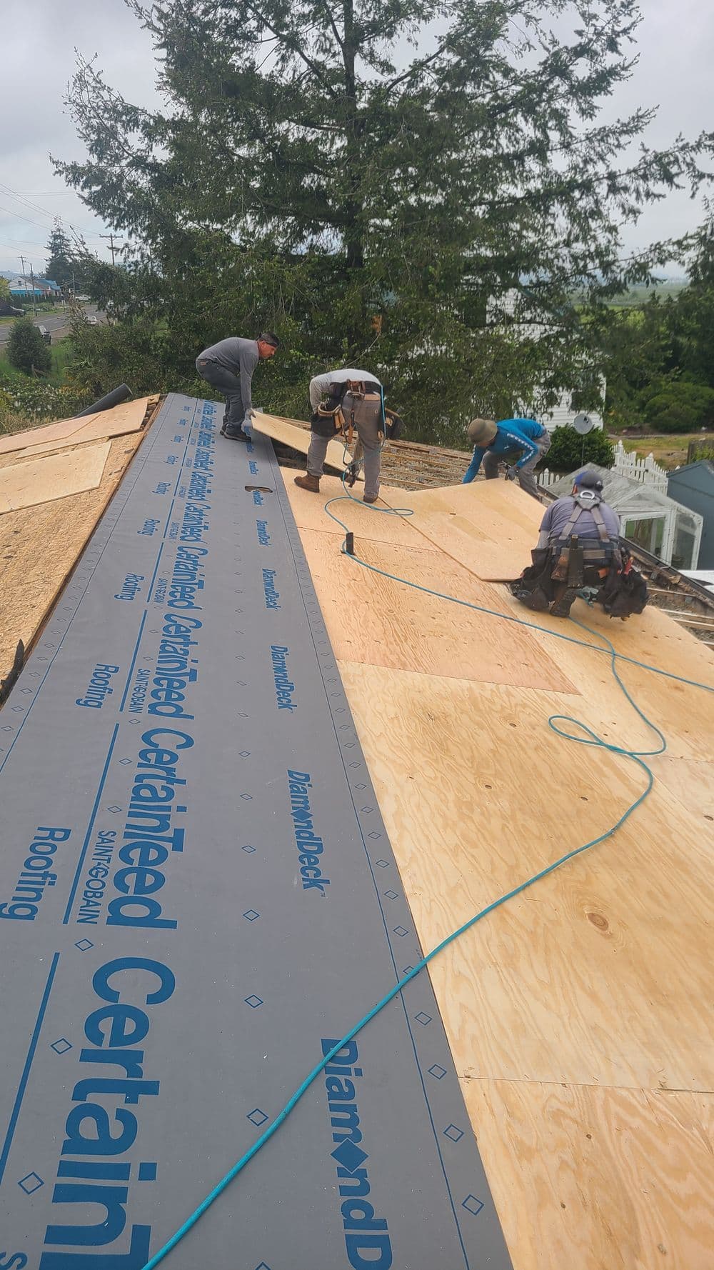 Contractors installing CertainTeed roofing on a sloped residential roof with tools and materials.