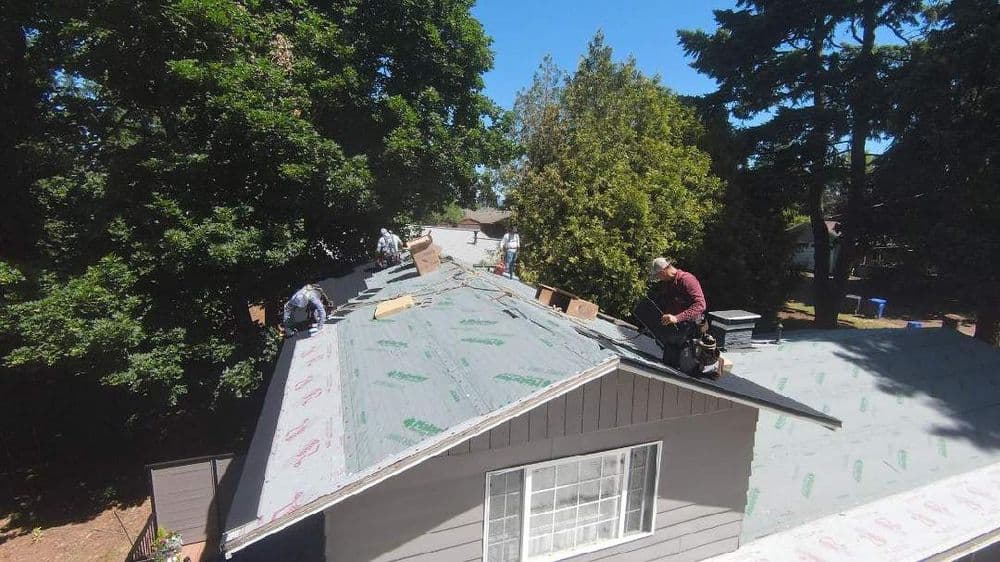Roofers installing shingles on a residential home under clear blue skies.