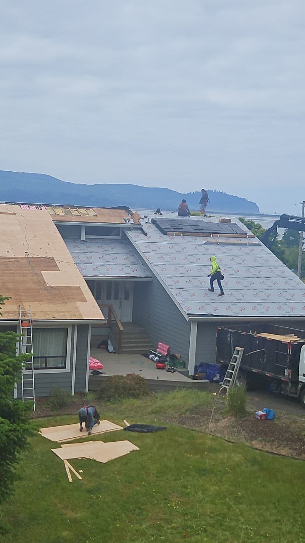 Workers installing a new roof on a house with mountains in the background.