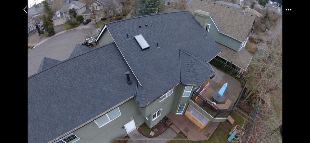 Aerial view of a residential home with a dark shingle roof and outdoor deck.