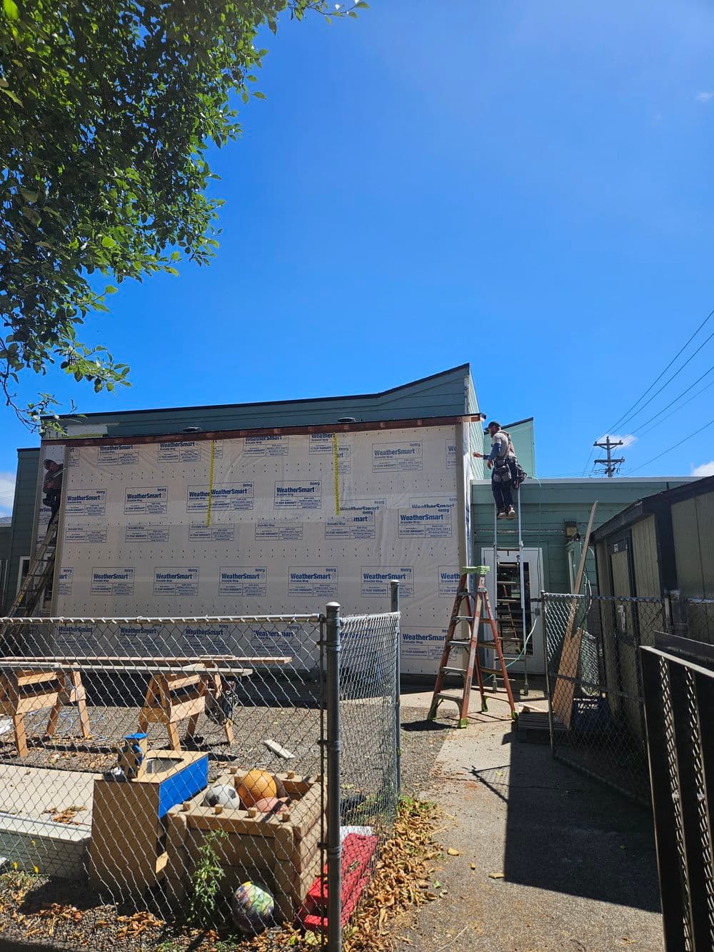 Construction worker installing exterior walls on a building under a clear blue sky.