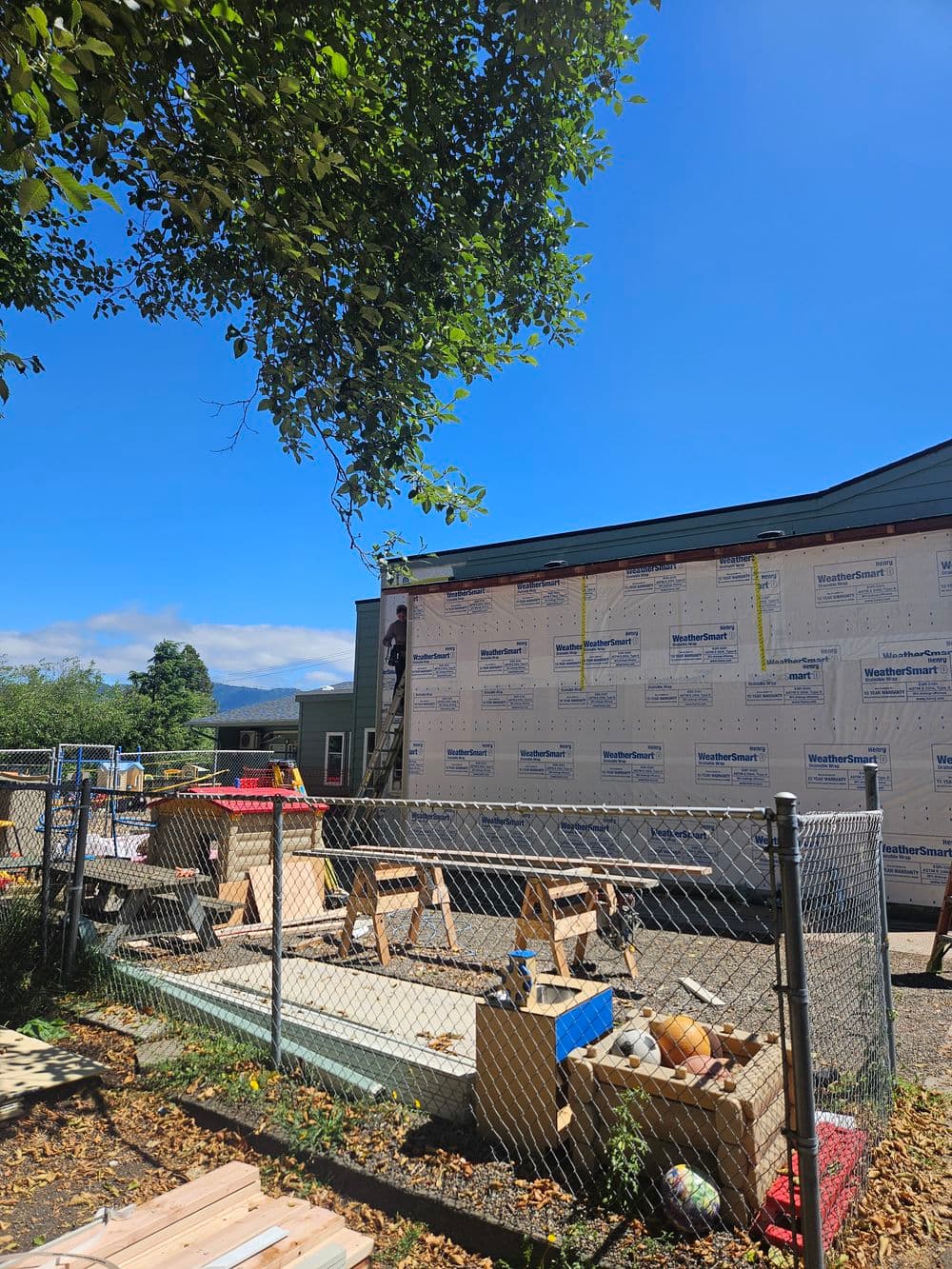 Construction site with building wrapped in insulation, scaffolding, and tools visible.