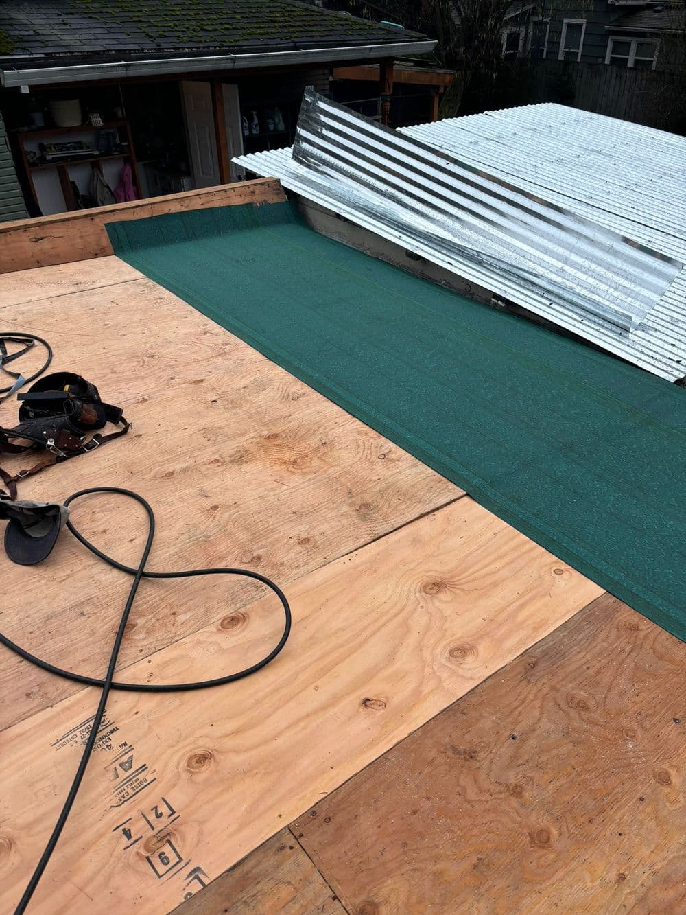 Roofing project with green underlayment, wooden boards, and metal sheets on a house.