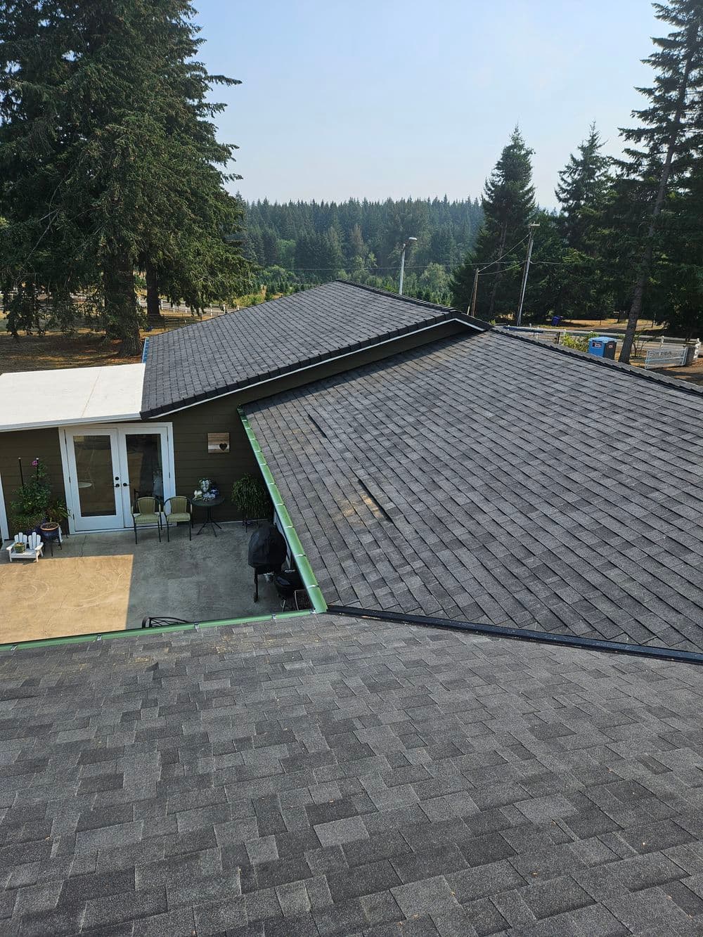 Aerial view of two sloped roofs with asphalt shingles, surrounded by trees.